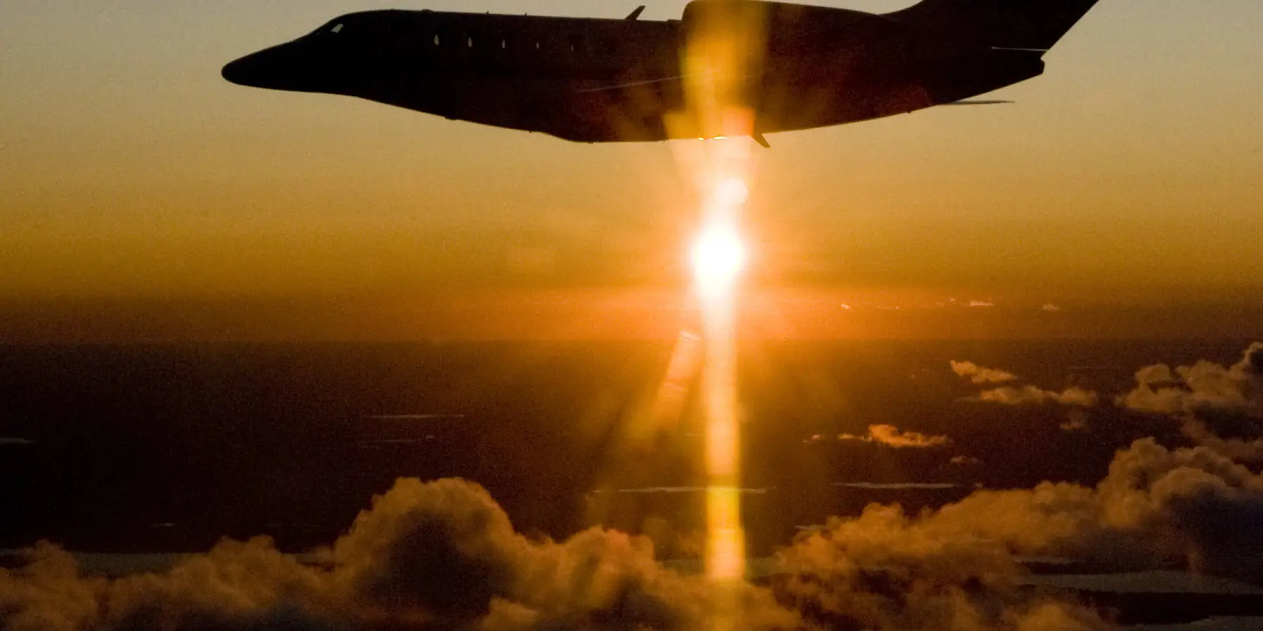 Citation X silhouetted against sunset above clouds